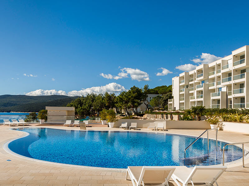 Little girl going down a slide at the Children's pool at Girandella Valamar Collection Resort, while her parents wait for her