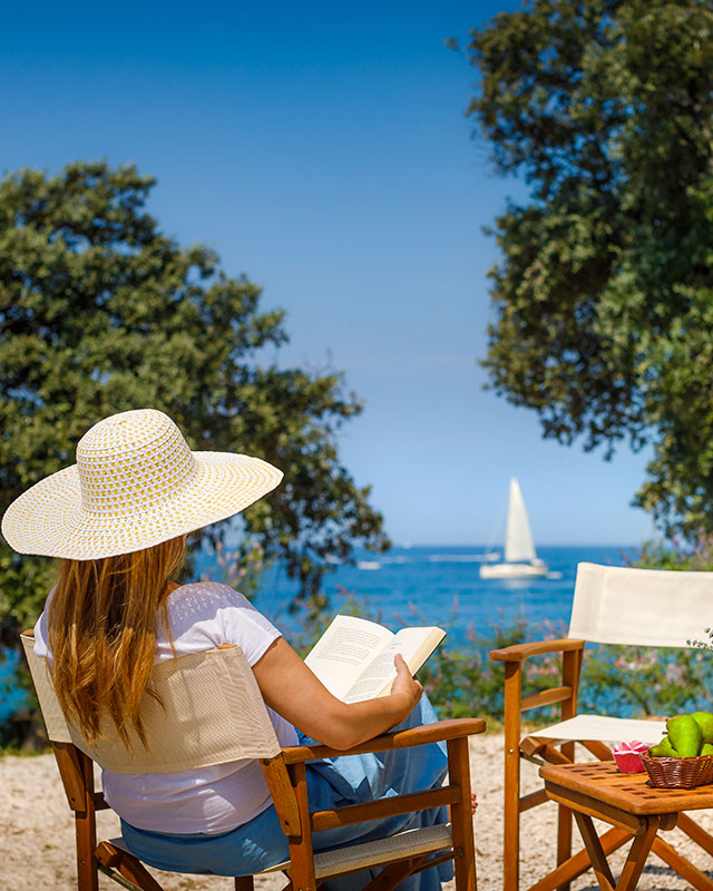 Donna che legge un libro e si rilassa sulla sua piazzola in prima fila sul mare.
