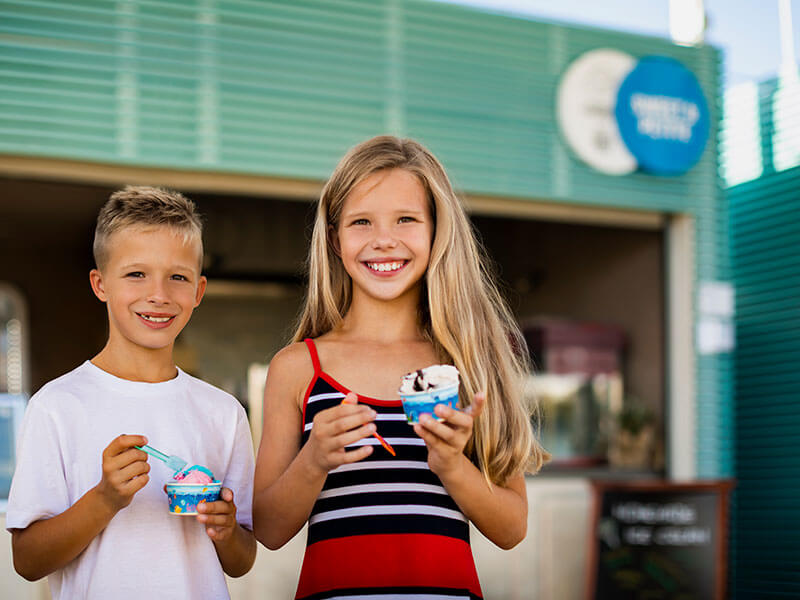 Due bambini che gustano un gelato davanti all’angolo gastronomico Piazza in un campeggio.