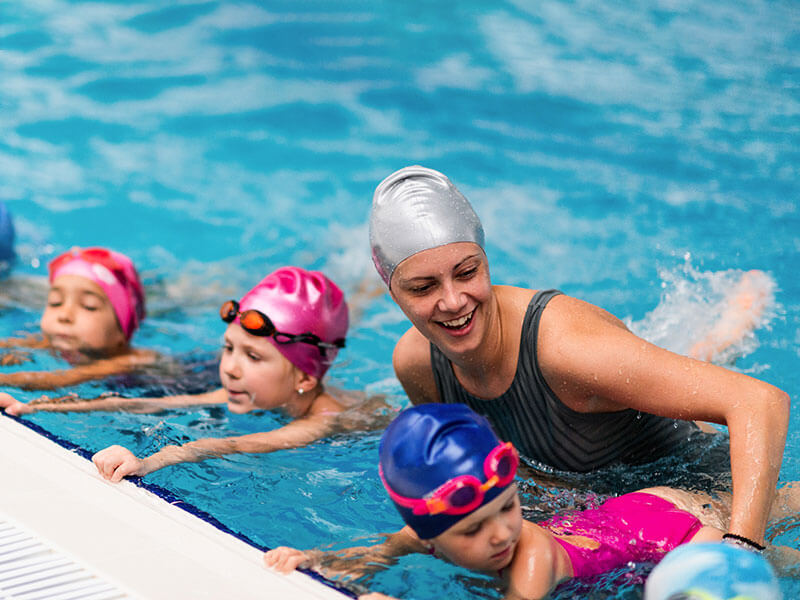 Swimming coach in the pool with a group of young children learning to swim at the Swimming Academy