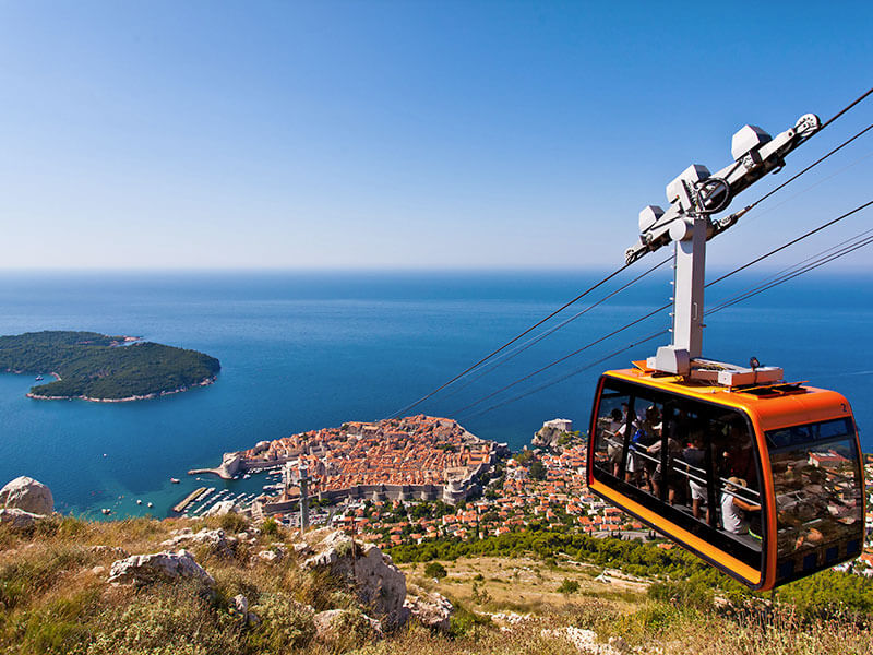 Red cable car ascending Mount Srđ with city and sea in background