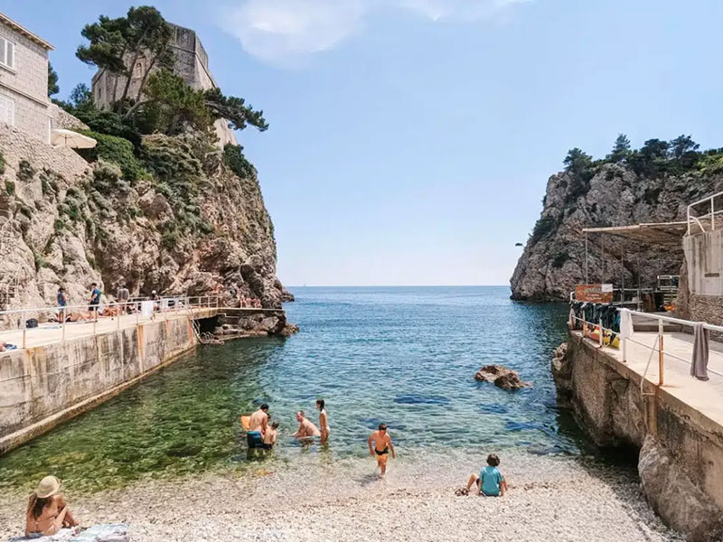 Malá skalnatá zátoka s plavci a kamennými zdmi u starého města Dubrovníku
