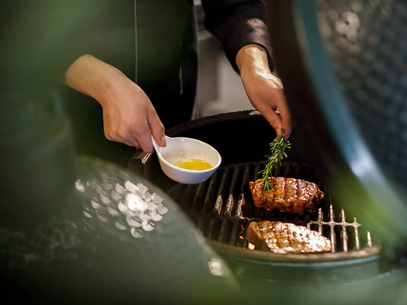 Chef che prepara una bistecca con olio d'oliva e rosmarino sulla griglia