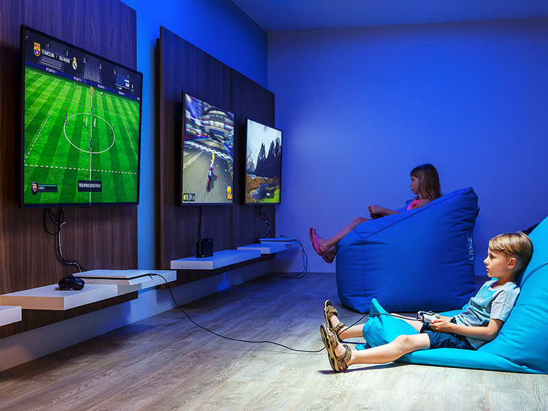 Un petit garçon et une fille, assis dans des poufs, jouent à des jeux sur Play Stations dans le Game Lounge du Girandella Valamar Collection Resort