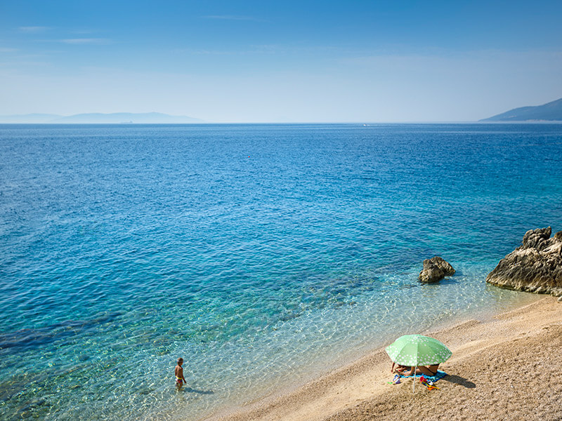 Widok z lotu ptaka na plażę Val Maro z leżakami i parasolami oraz Poreč w tle.