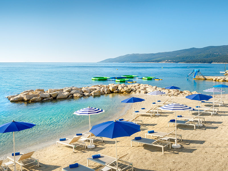 Leżaki i parasole na piaszczystej rodzinnej plaży Val Sundance z dmuchanym parkiem wodnym Wibit w tle