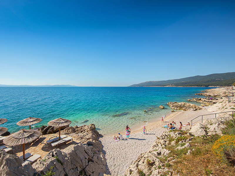 Ležaljke na stjenovitom brežuljku s pogledom na šljunčanu plažu Val Sunrise Relax