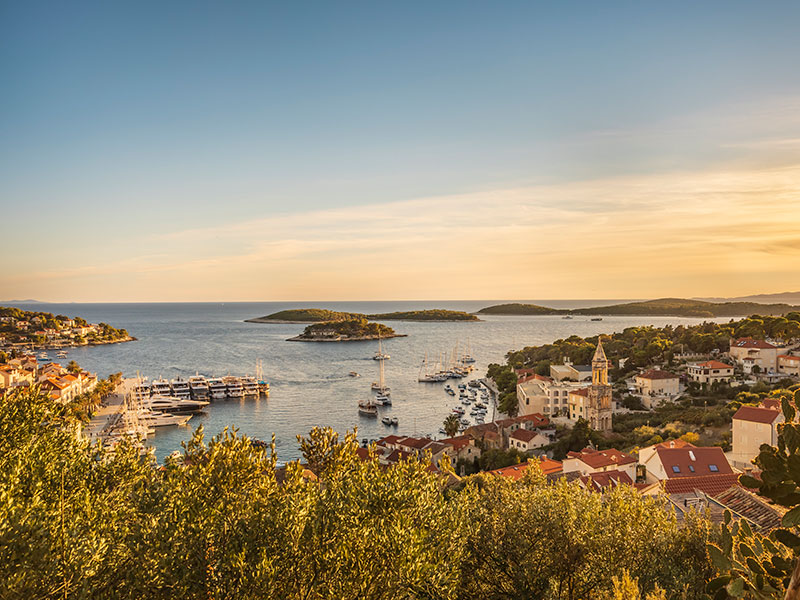 Zračni pogled na obalo Hvara s pristaniščem, čolni in starim mestnim jedrom ob sončnem zahodu