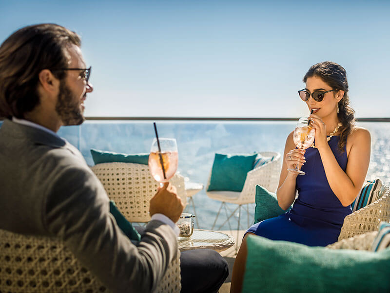 Paar trinkt Cocktails auf der sonnigen Terrasse der Miramare Lobby Bar mit Meerblick.