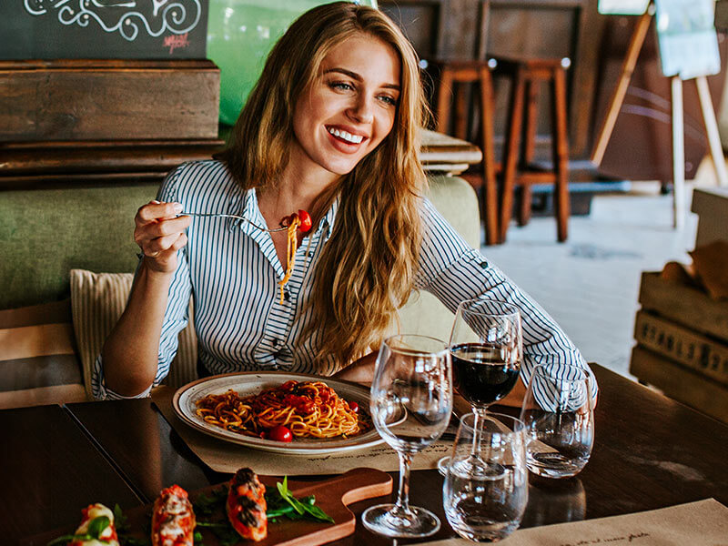 Donna che mangia pasta e bruschette e beve vino in un ristorante.