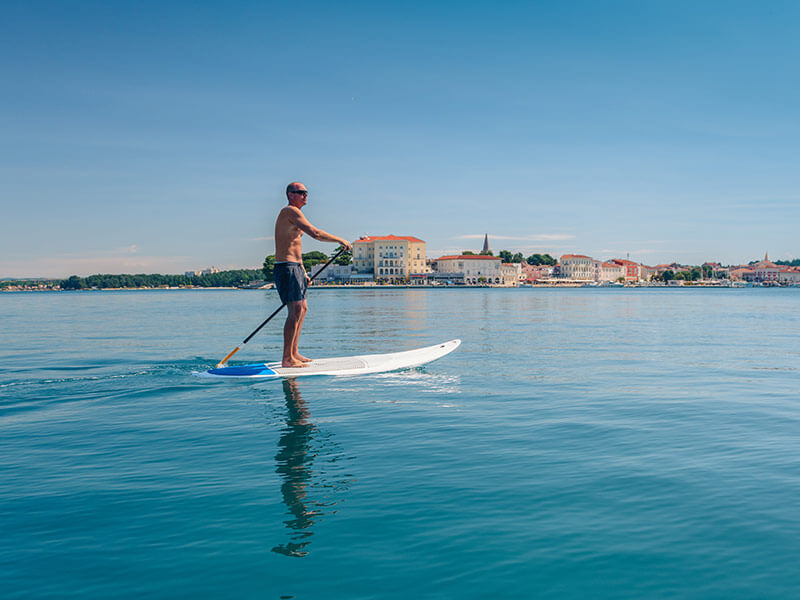 Muškarac vesla na SUP-u s Porečom u pozadini.