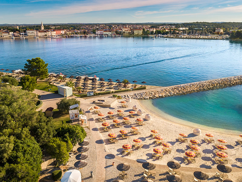 Zračni pogled na pješčanu plažu Val Maro s ležaljkama i suncobranima te Poreč u pozadini.