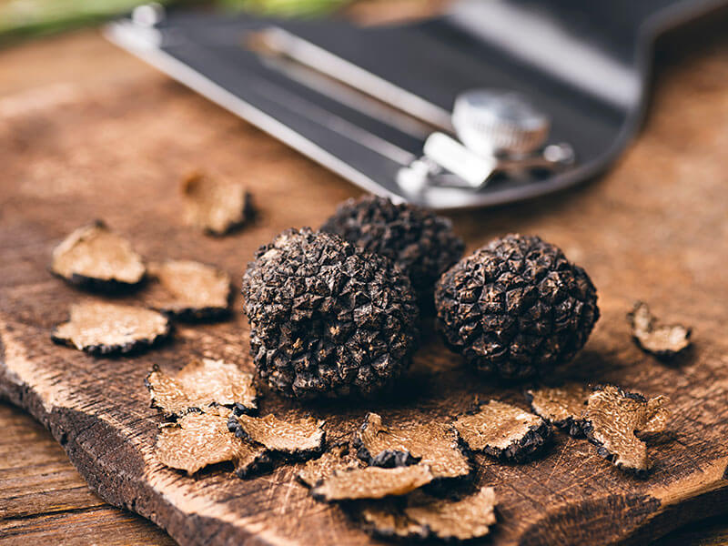 Black truffles and slices on wooden board