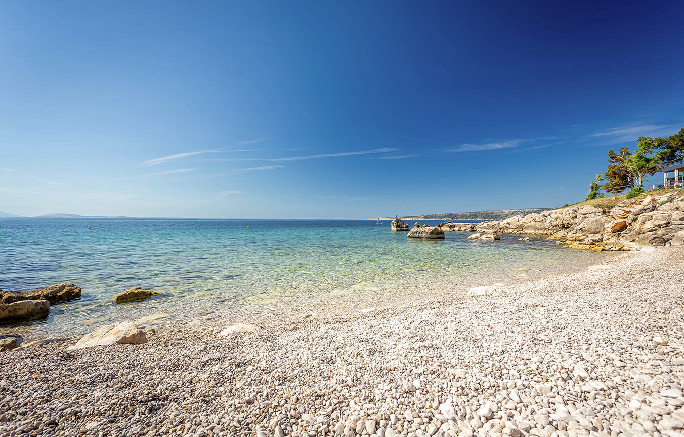Kamienista plaża z leżakami i parasolami nad czystym Adriatykiem