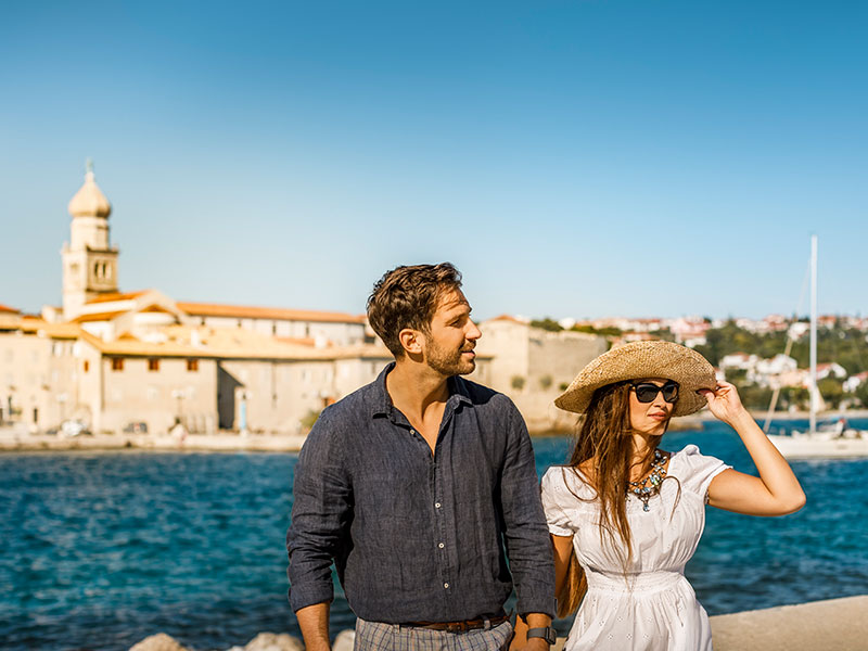 Turistički par stoji na obali u luci Krk s pogledom na stari grad u pozadini