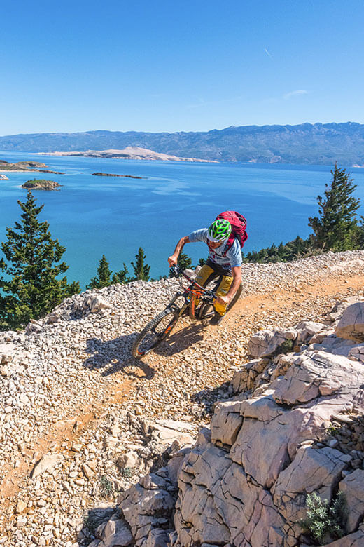 Cyclist riding a mountain trail with panoramic views of the Adriatic Sea and Kvarner islands in Croatia.