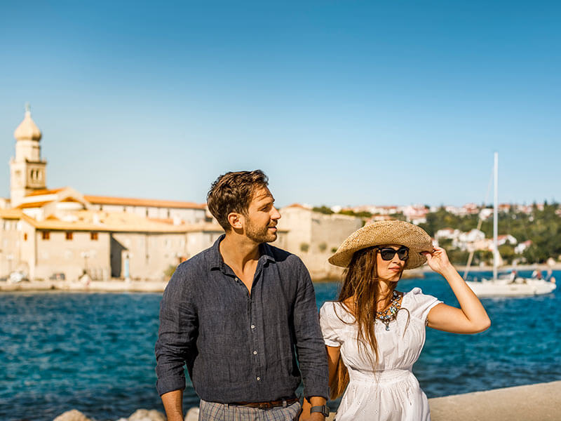 Couple walking by the sea in Kvarner, with Krk Town in the background