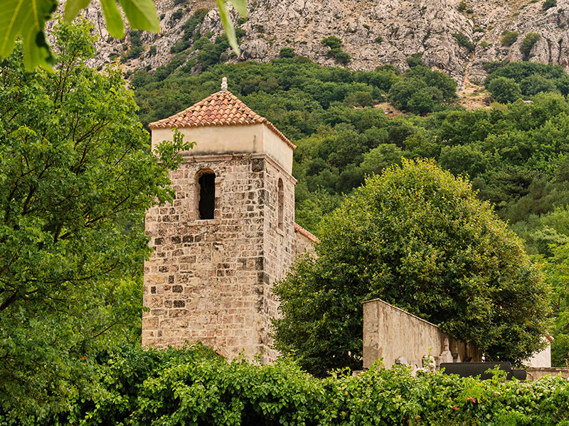 Historic stone church tower surrounded by greenery and mountains in Kvarner.