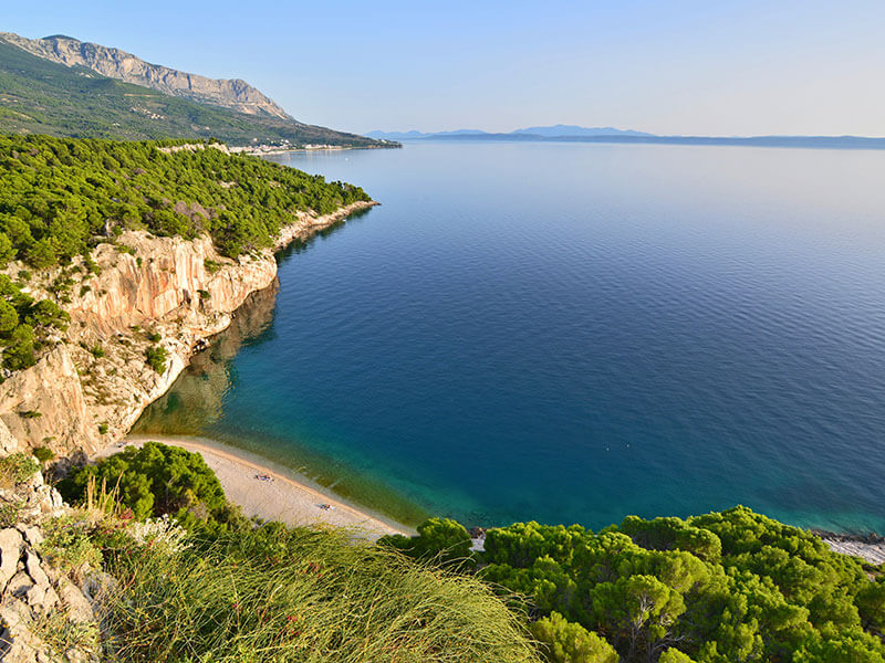 Secluded nudist FKK beach in Makarska surrounded by rocky terrain and forest