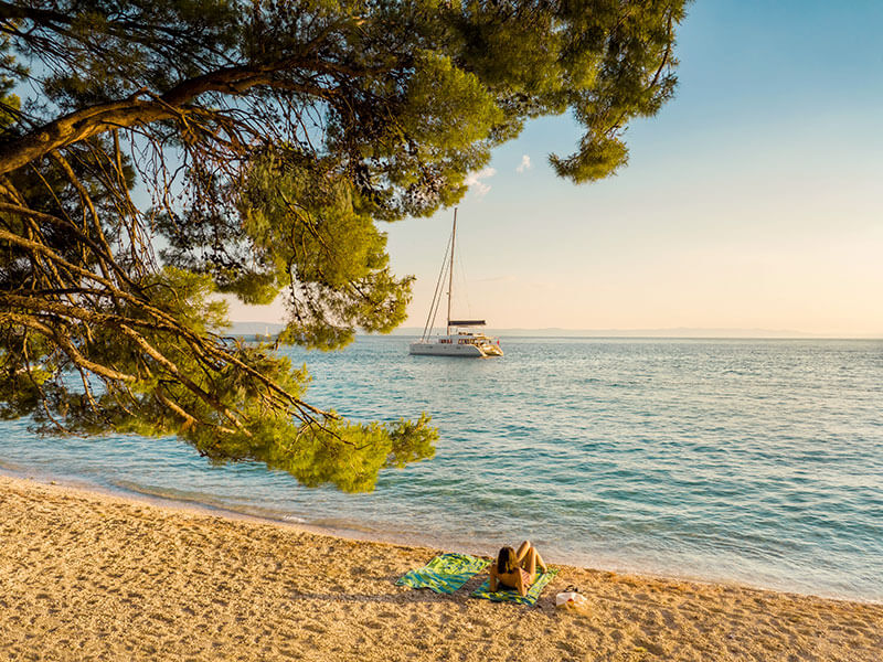 Plage de galets à Makarska ombragée par des pins avec un voilier en vue