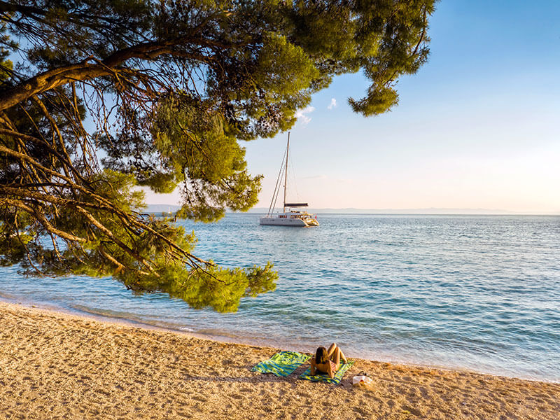 Town Beach in Makarska with pine shade and sailboat views