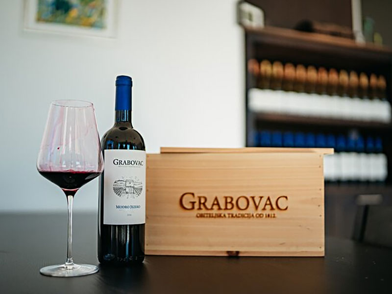 Bicchiere di vino rosso e bottiglia Grabovac accanto a scatola di legno con marchio