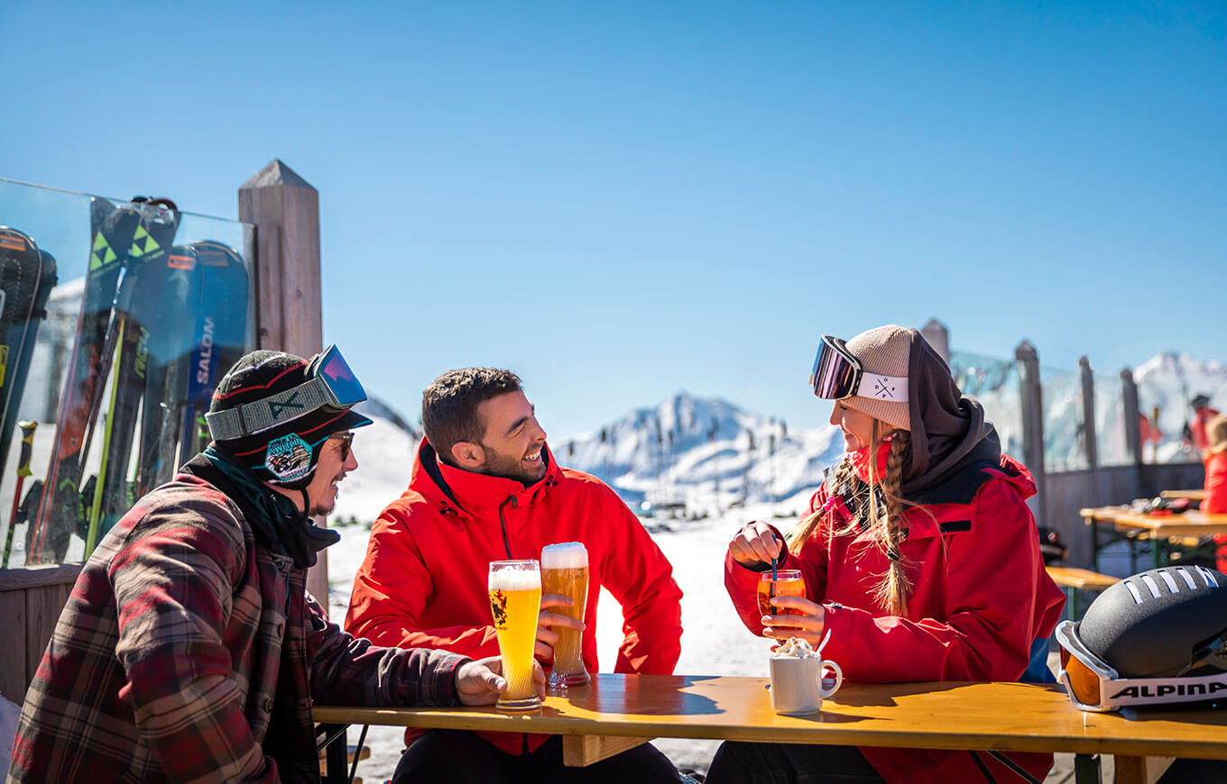 Traja priatelia sedia v après-ski bare na vrchole najsnežnejšieho lyžiarskeho strediska v Rakúsku