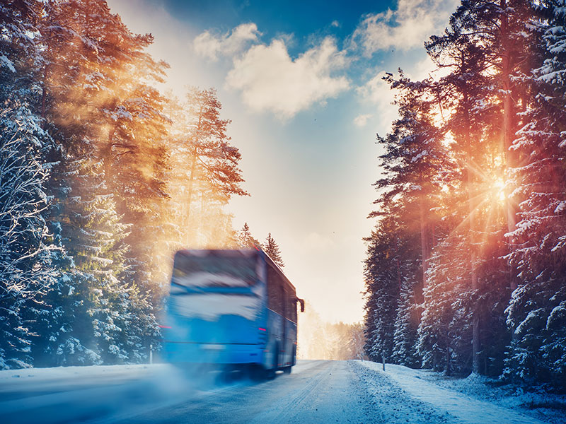 Bus fährt bei Sonnenaufgang auf einer verschneiten Waldstraße