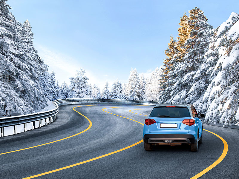 Auto fährt auf einer schneebedeckten Bergstraße, umgeben von winterlichen Bäumen, auf dem Weg nach Obertauern