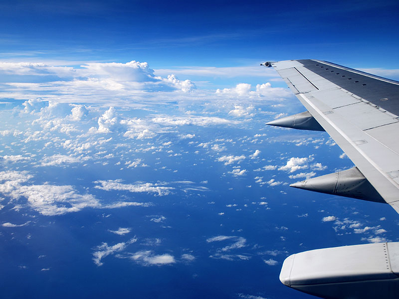 Blick aus dem Flugzeugfenster auf den Flügel über einem Wolkenmeer