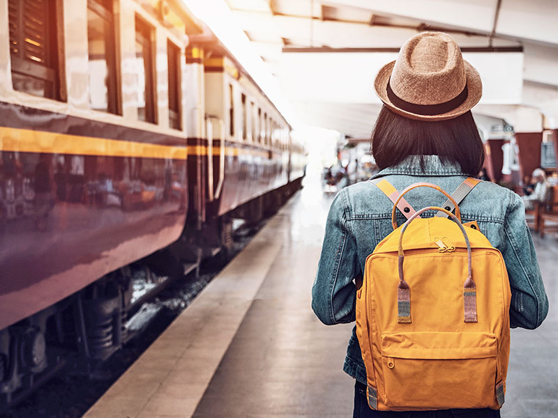 Reisender mit gelbem Rucksack und Hut steht auf dem Bahnsteig
