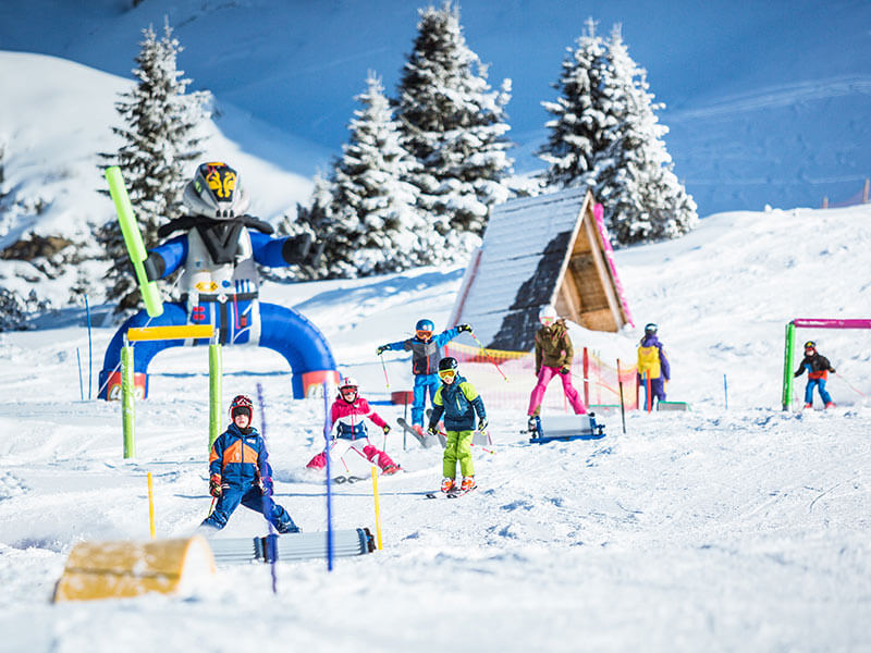 Kinder lernen Skifahren im Frau Holle Kinderland in Obertauern und fahren durch bunte Hindernisse auf einer verschneiten Piste