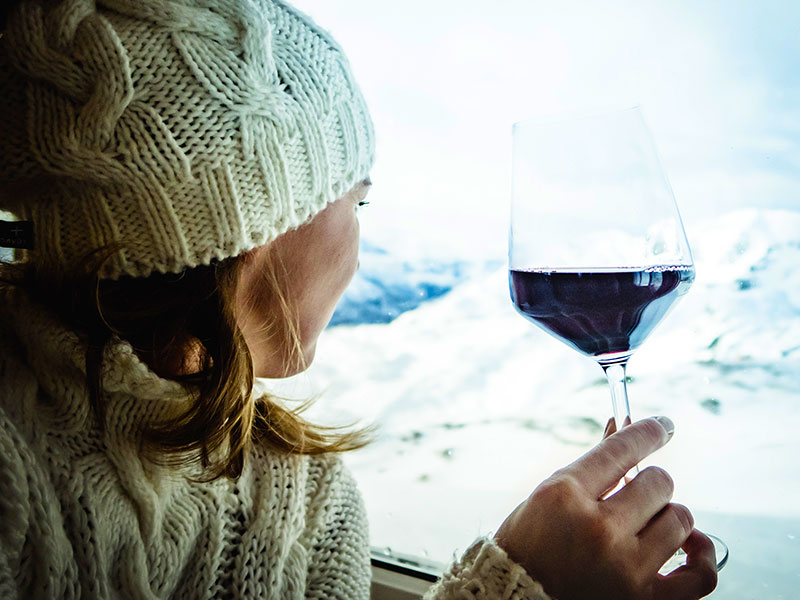 Frau trinkt ein Glas Wein mit Blick auf die verschneiten Gipfel