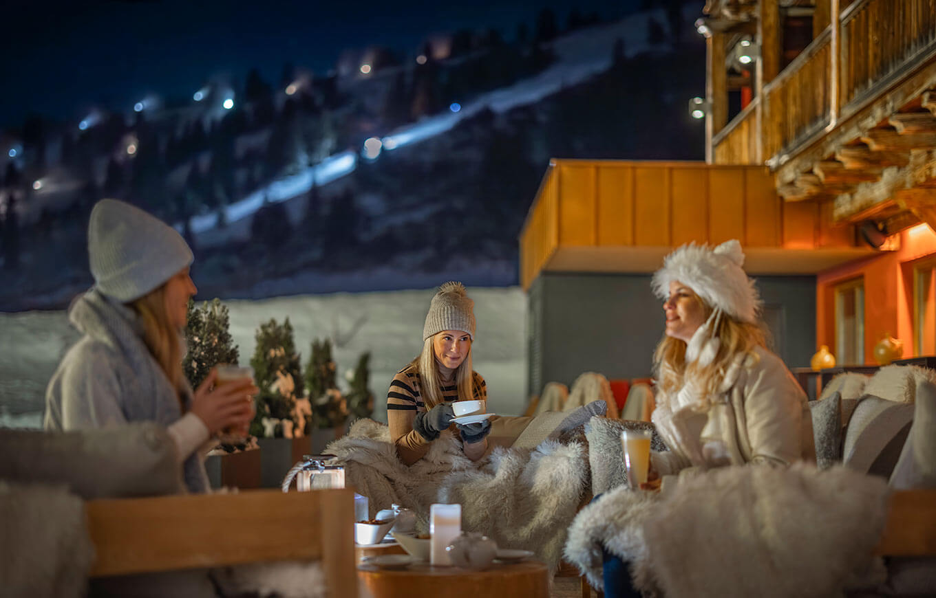 Traja priatelia si vychutnávajú après-ski drinky pred hotelom Kesselspitze, Valamar Collection