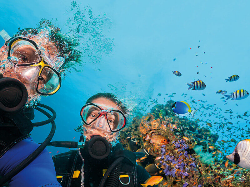 Underwater selfie of two scuba divers near vibrant coral reef