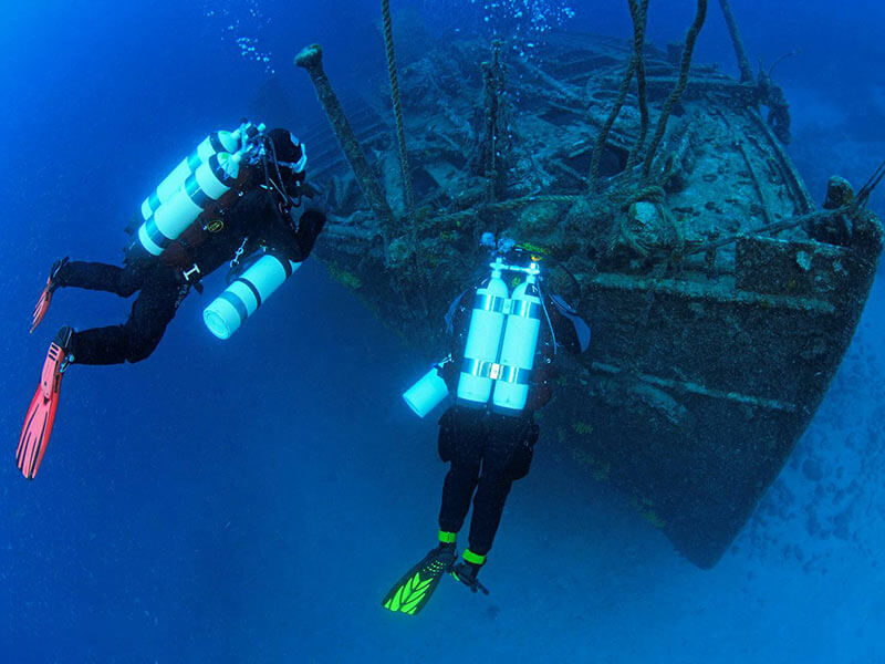 Two scuba divers inspecting a large sunken shipwreck
