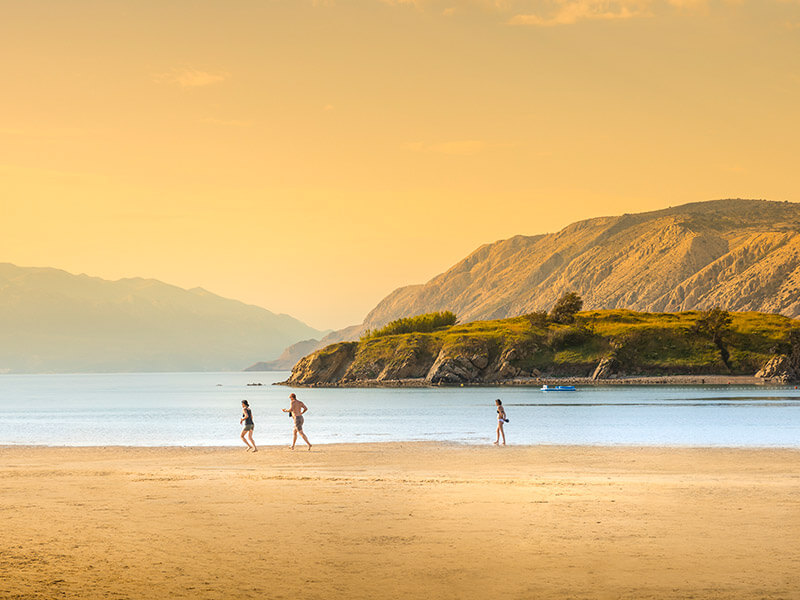 Menschen spazieren bei Sonnenuntergang über einen breiten Sandstrand auf der Insel Rab