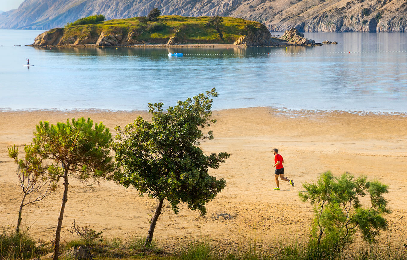 Un homme court sur la plage de sable Paradise avec les falaises de Rab au loin