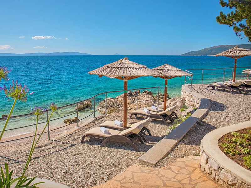 Stylish beach terrace with loungers and parasols above turquoise sea
