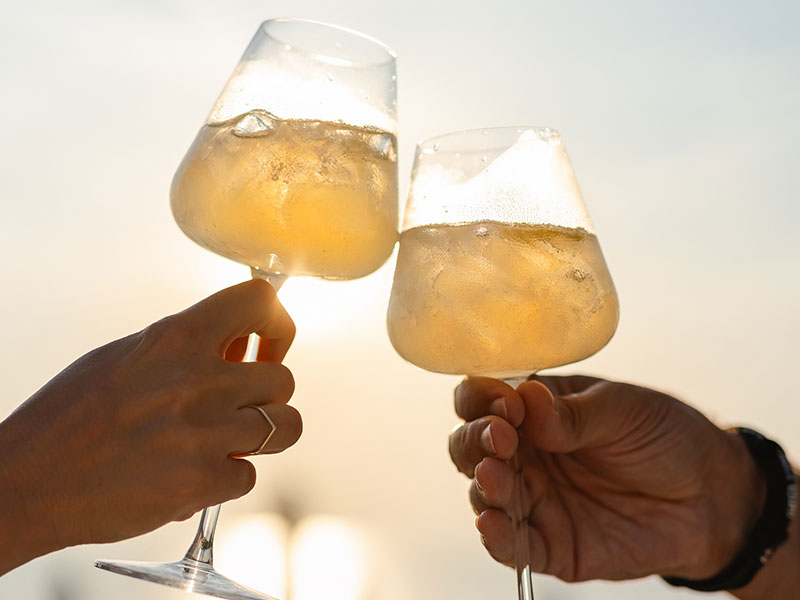 Zbliżenie dwóch osób wznoszących toast koktajlami o zachodzie słońca