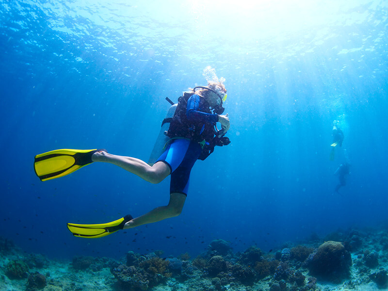 Taucher schwebt im klaren blauen Wasser, während Sonnenstrahlen von oben einfallen