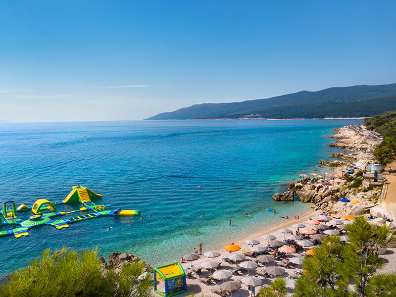 Family beach with pine trees and gentle waves in Rabac