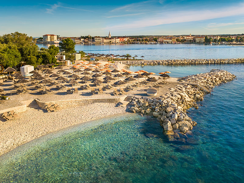 Šljunčana plaža Val Sunrise Family Beach s ležaljkama i suncobranima.