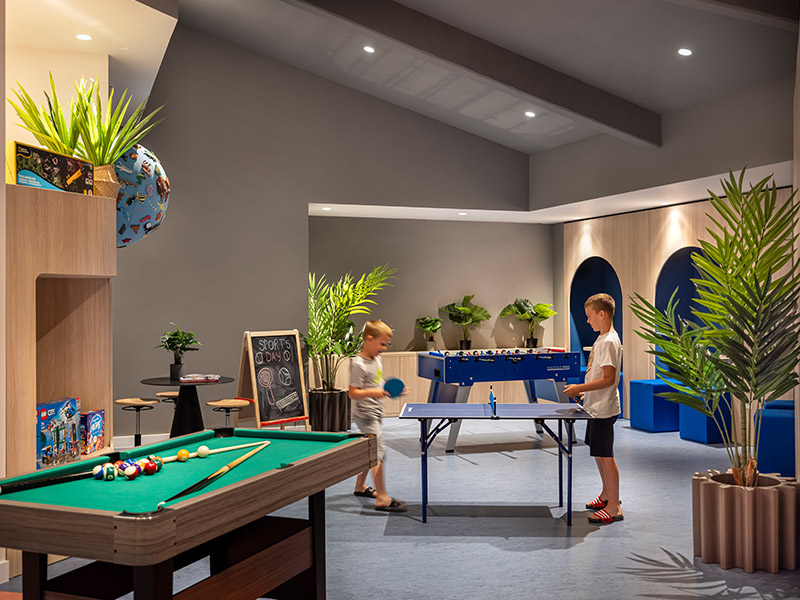 Ein kleiner Junge und ein Mädchen sitzen in Sitzsäcken und spielen Spiele auf PlayStations in der Game Lounge des Girandella Valamar Collection Resort