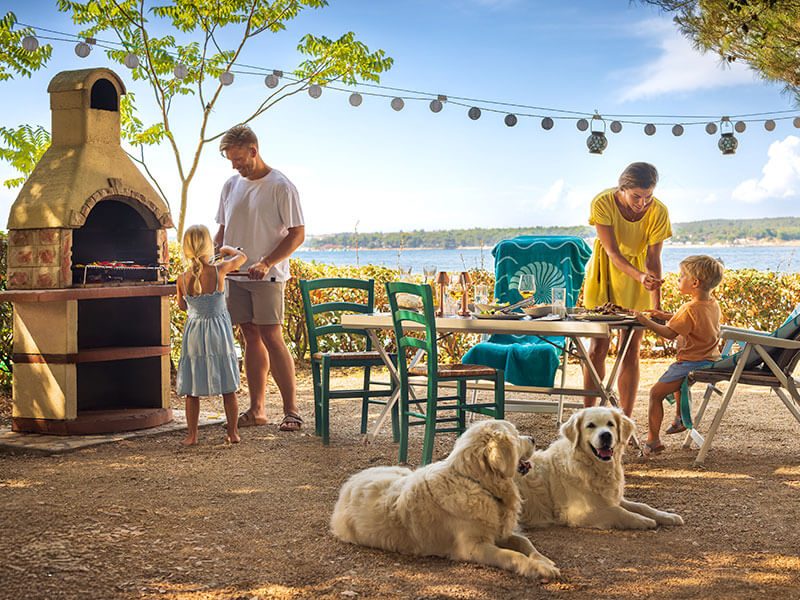 Famille profitant d'un barbecue dans un camping en bord de mer en Croatie avec des chiens.