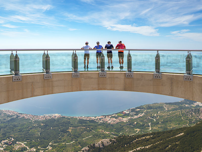 Group of cyclists standing on the Biokovo Skywalk, enjoying panoramic views of the Adriatic coast and mountains in Croatia