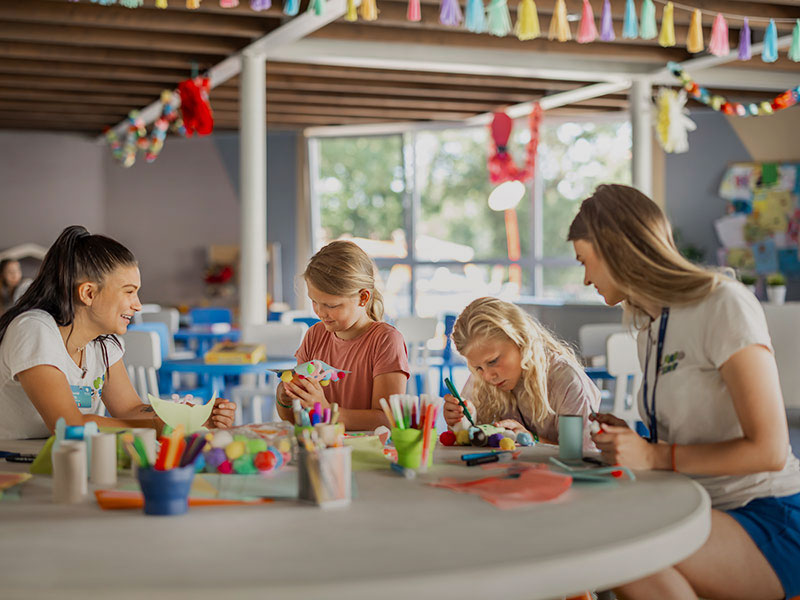 Kinder basteln mit Papier an einem Tisch, betreut von Maro-Babysittern.