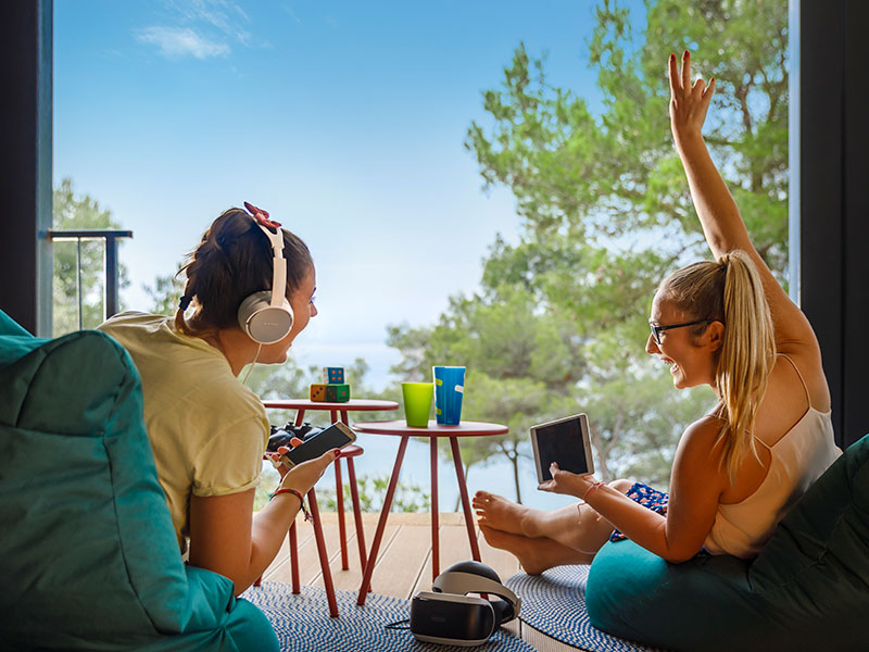 Two teenage girls playing on gaming consoles in bean bags 