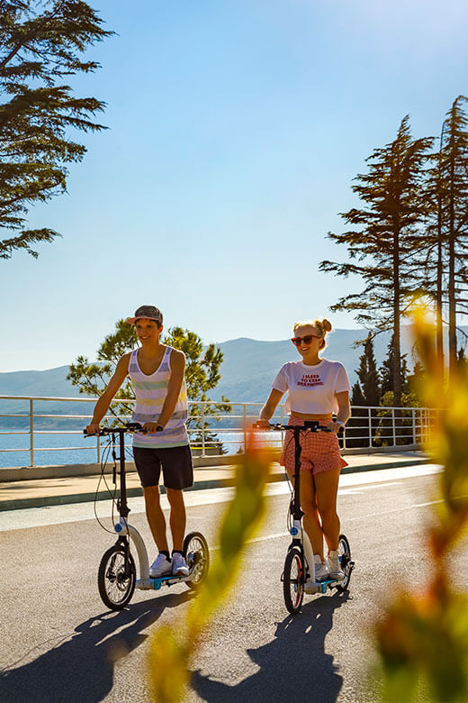 Two teens riding scooters on a seaside road in Croatia