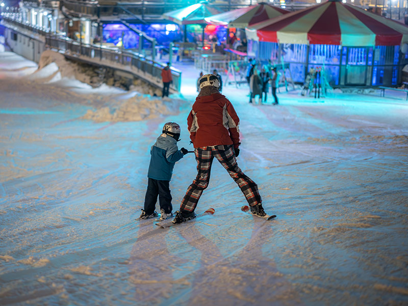 Elternteil und Kind fahren nachts Ski während eines Familienwinterurlaubs in Österreich.